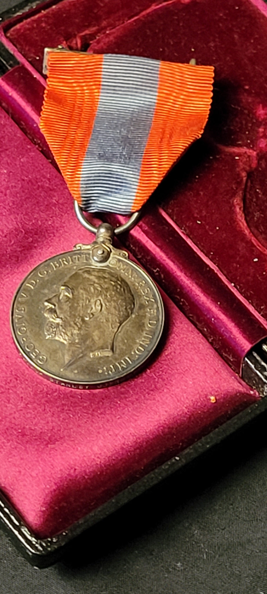 A silver-toned commemorative medal with an orange, white, and blue striped ribbon, displayed inside a dark red velvet-lined presentation box.