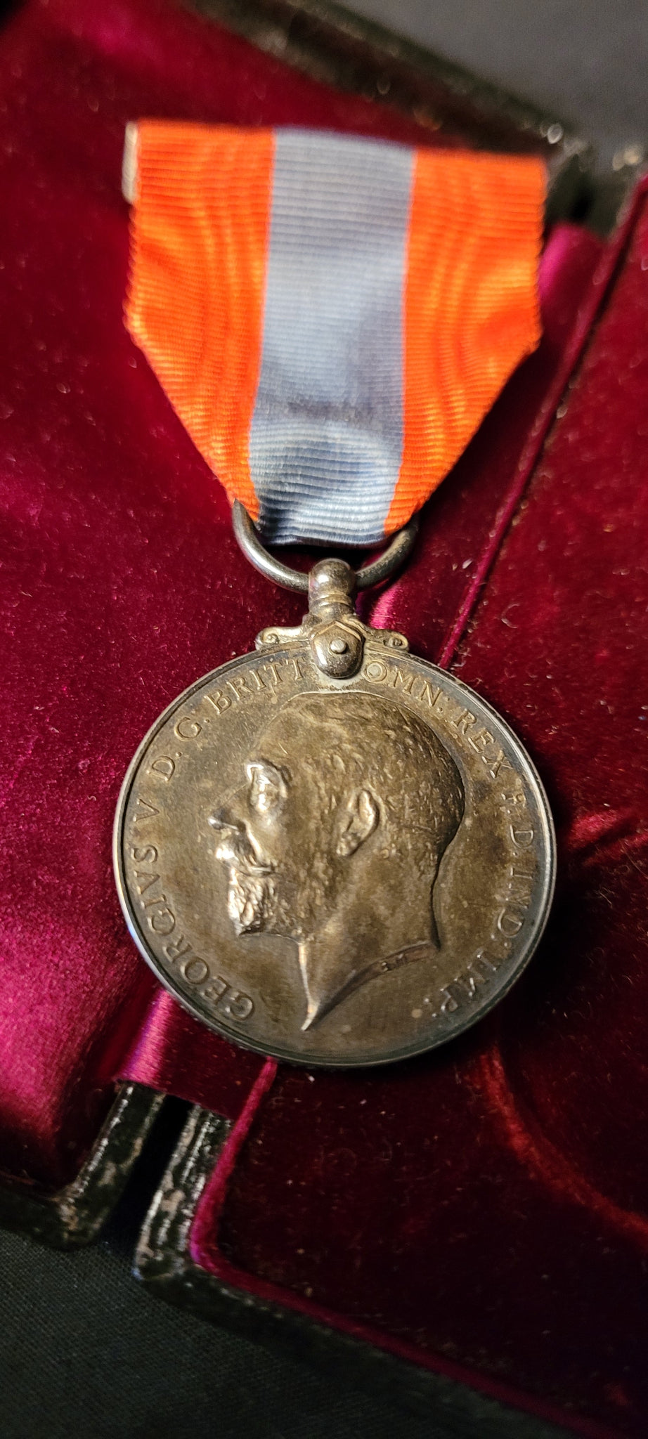 A silver-toned military medal with an red and blue ribbon, displayed inside a red velvet box.